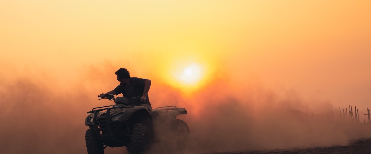 Quad ATV pędzi w chmurze pyłu polną drogą o zachodzie słońca